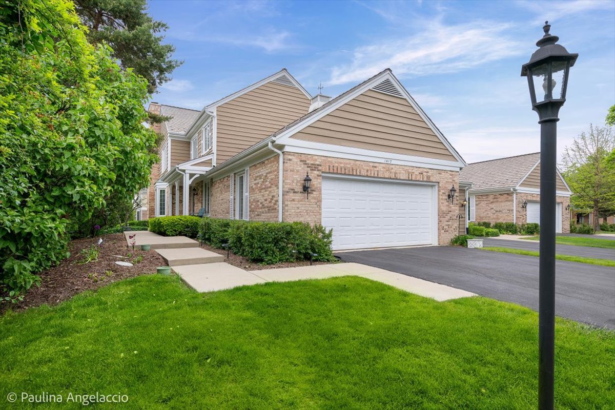 Two-story tan-and-brick home with a double garage, landscaped walkway, and black lamp post.