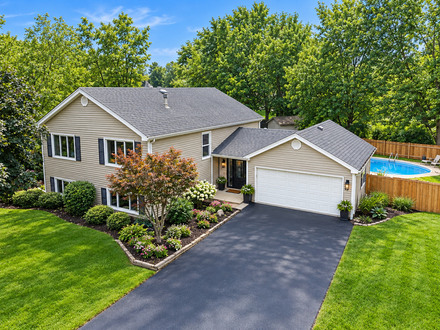 Two-story beige home with attached garage, landscaped front yard, and fenced backyard pool.