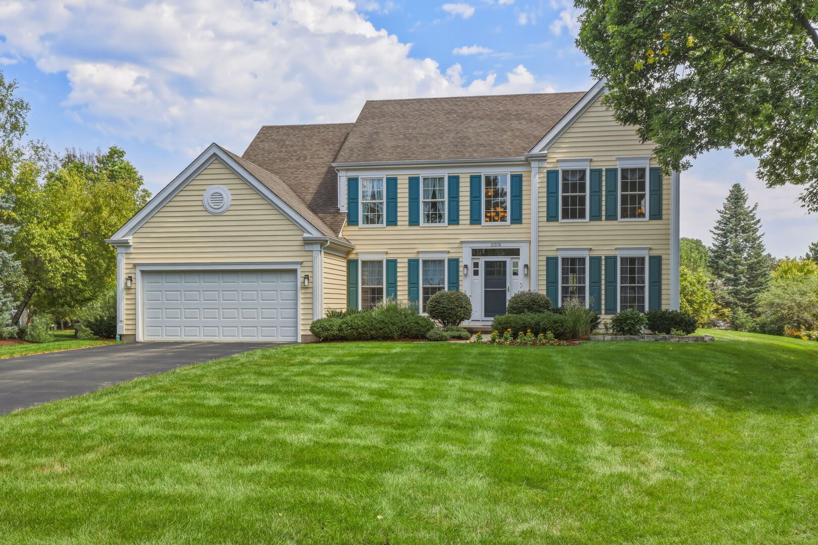 Two-story yellow home with teal shutters, a double garage, and a broad green lawn.