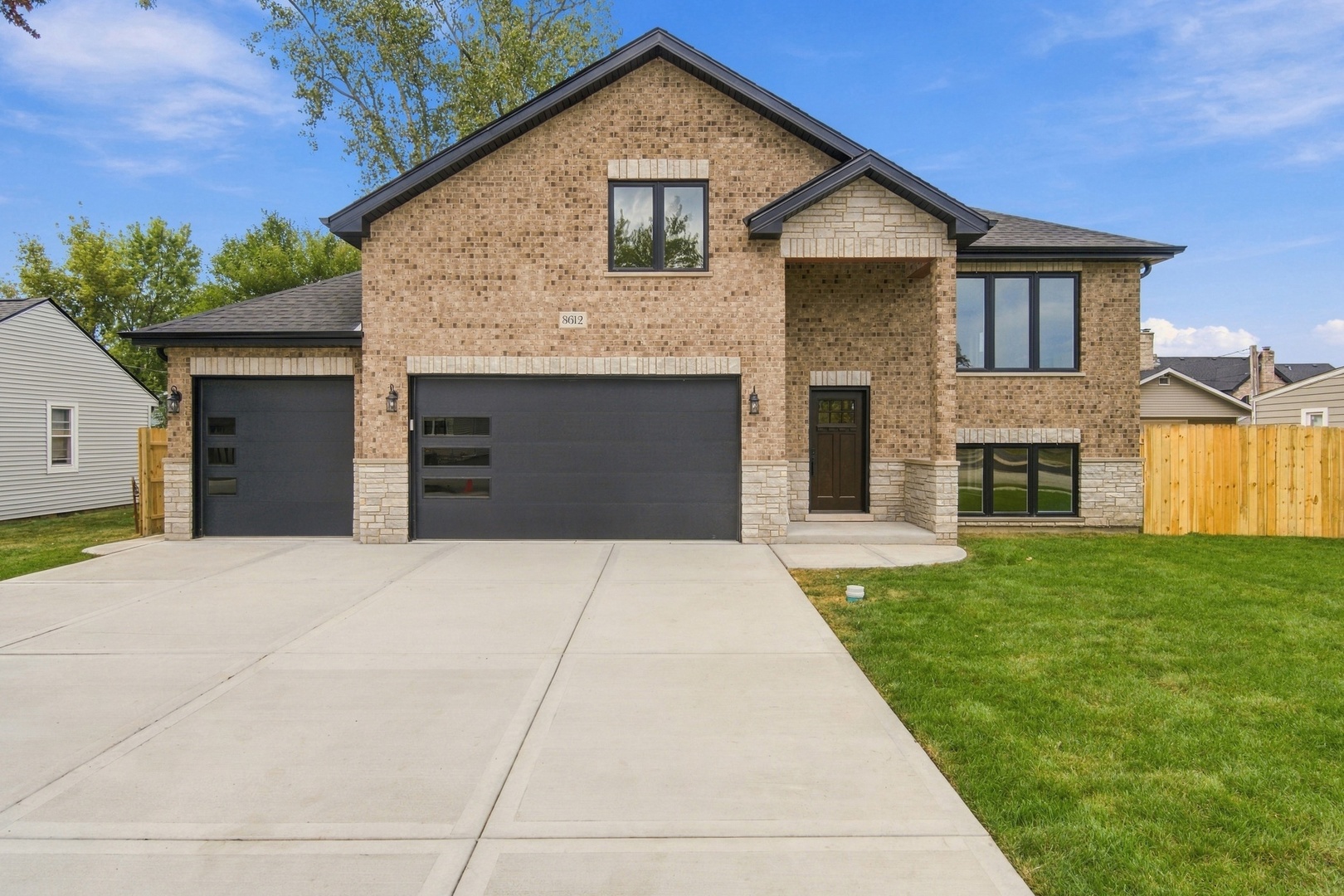 Two-story brick home with dual dark garage doors, stone accents, and a wide concrete driveway.