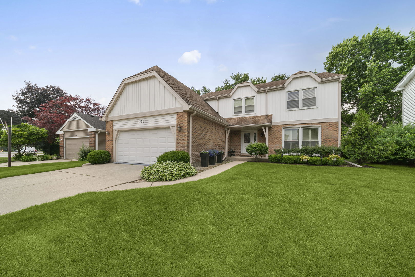 Two-story brick and white-sided house with a double garage and broad green lawn.