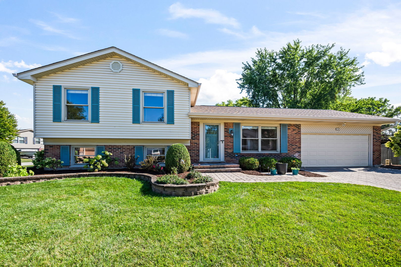 Split-level home with white siding, brick, blue shutters, and an attached two-car garage.