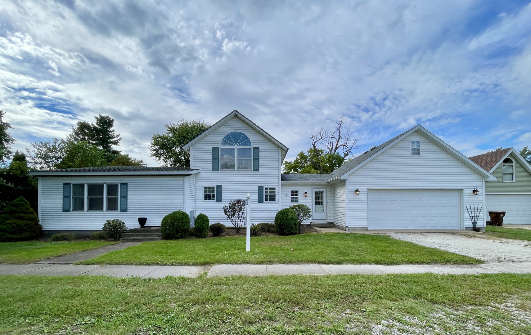 White two-story house with an arched upper window, attached garage, and green front lawn.