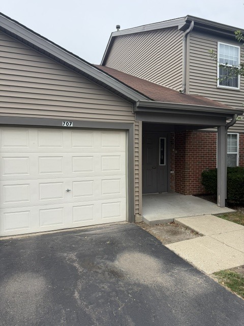 Attached home with a white double garage door, covered entry, and brick accents.