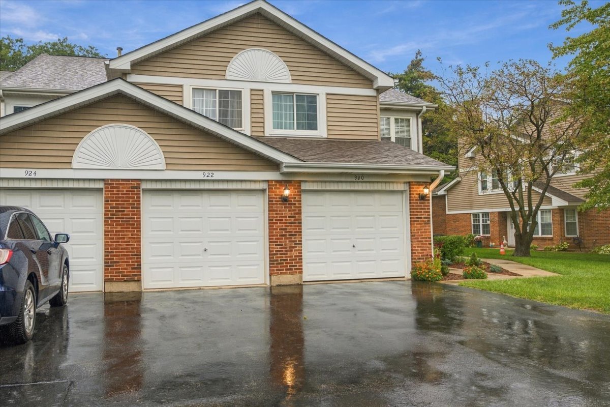 Attached homes with tan siding and brick accents, white garage doors, and a wet driveway.
