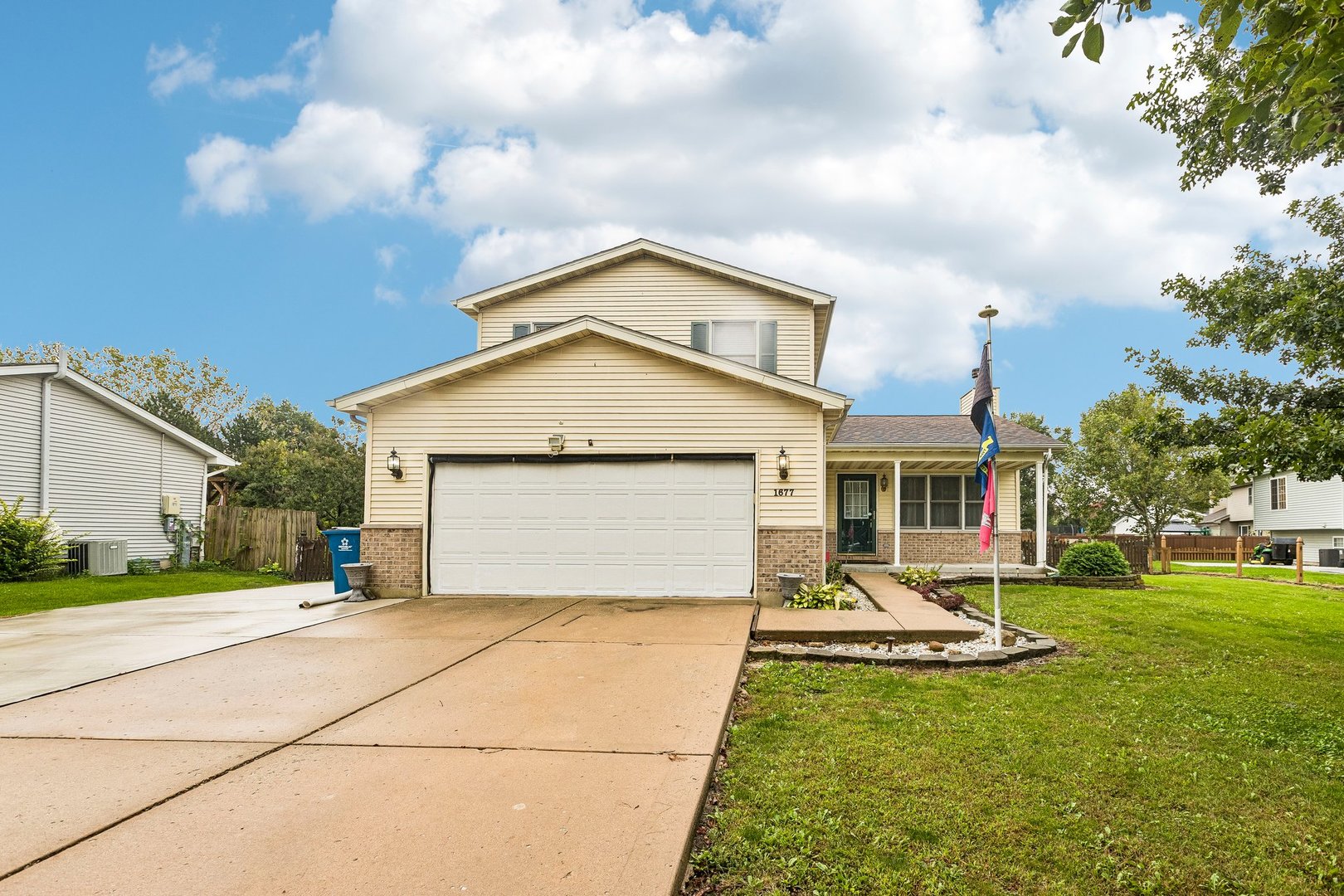 Beige two-story house with brick accents, a two-car garage, covered porch, and broad driveway.
