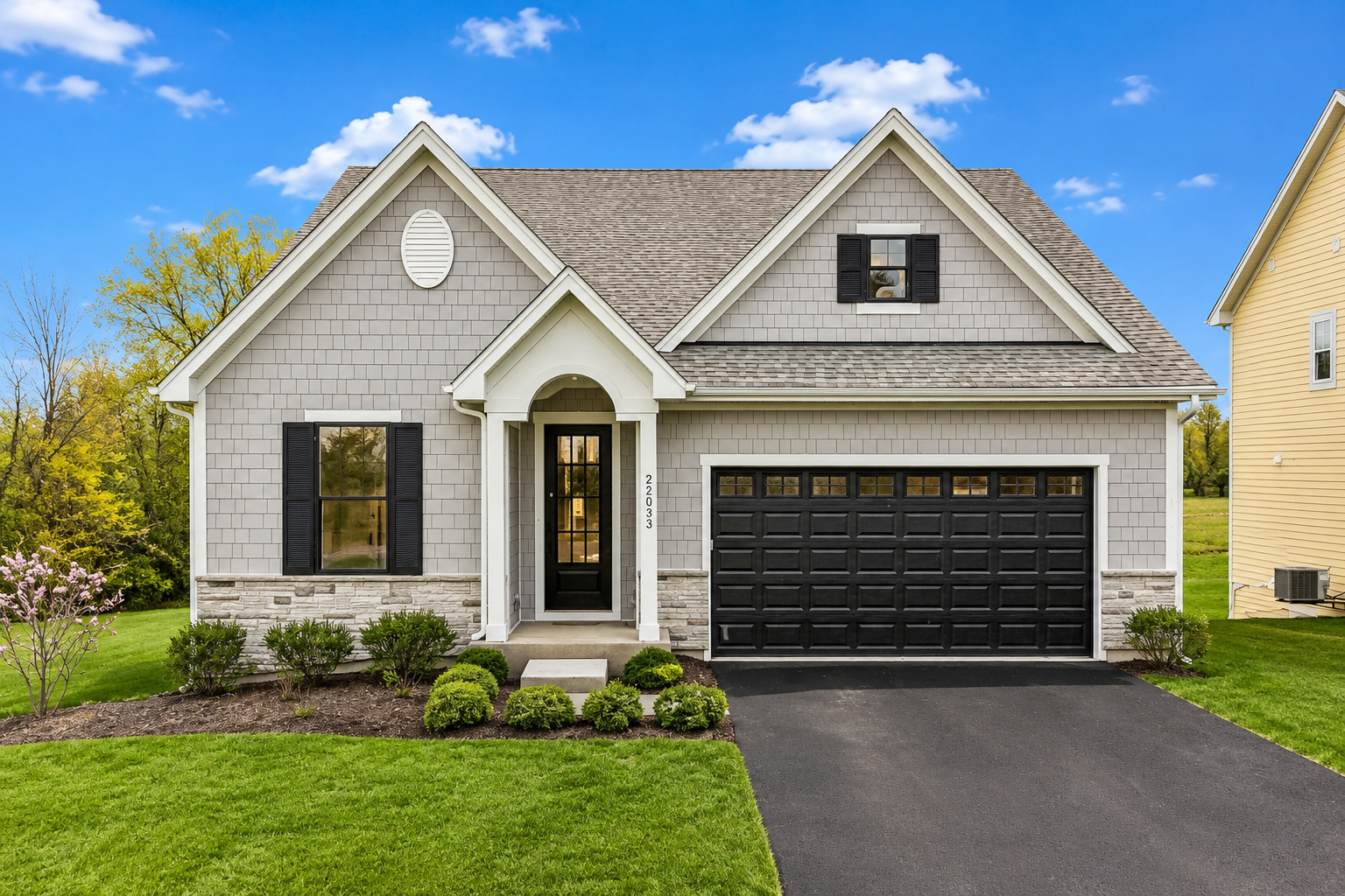 Gray-shingle home with black shutters, a covered entry, and a two-car garage.