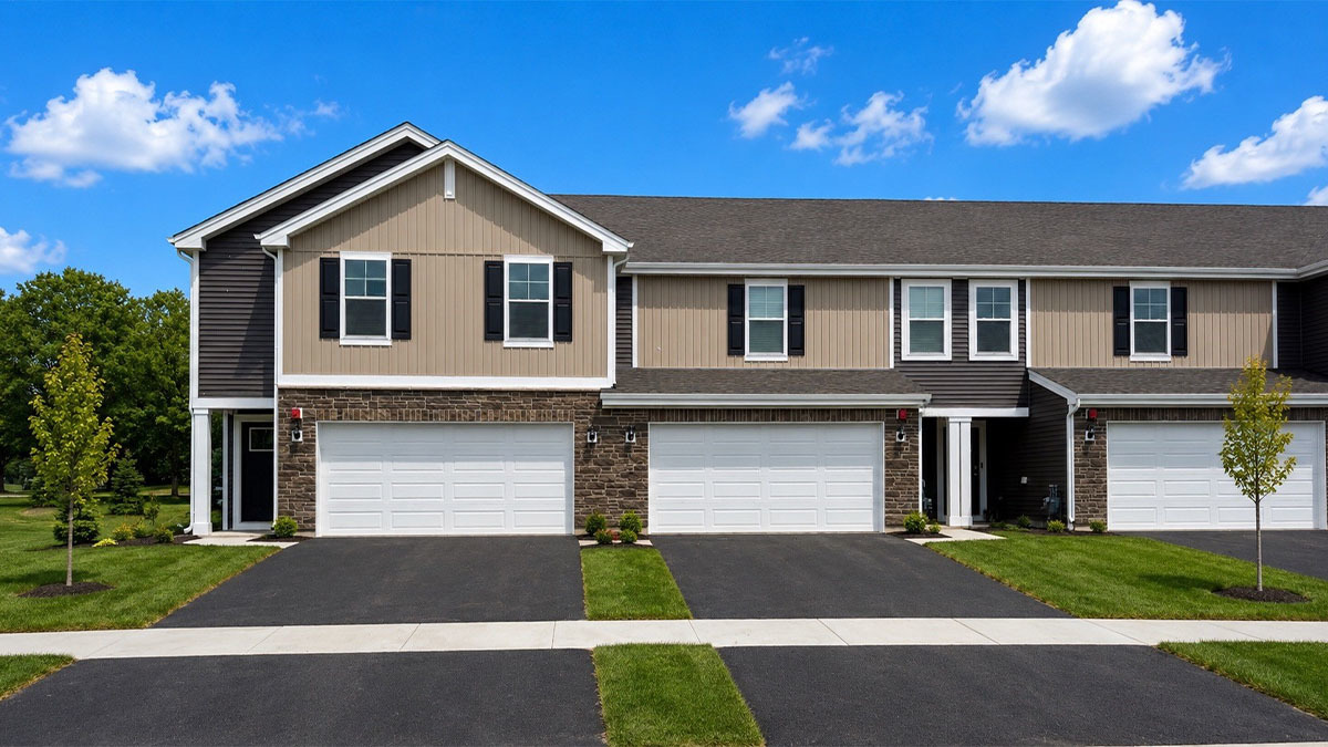 Attached tan homes with stone veneer, white garage doors, and landscaped lawns.