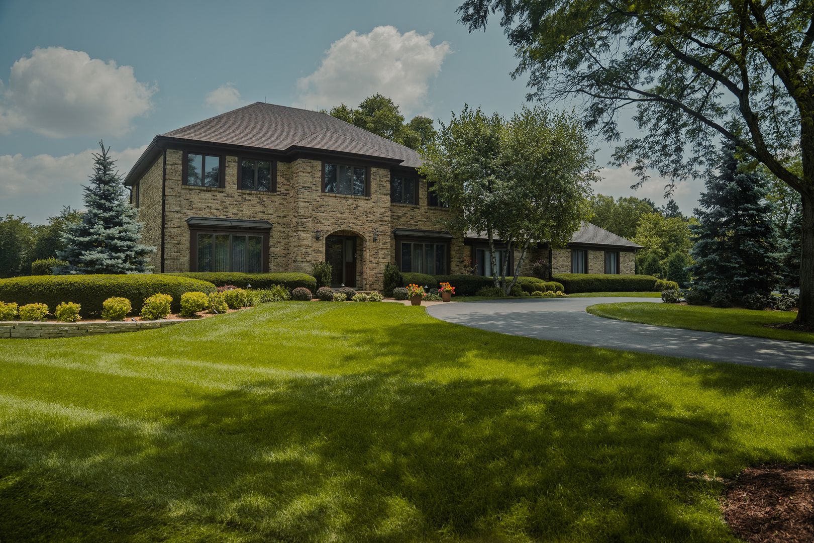 Two-story brick home with a curved driveway, landscaped lawn, and mature trees.