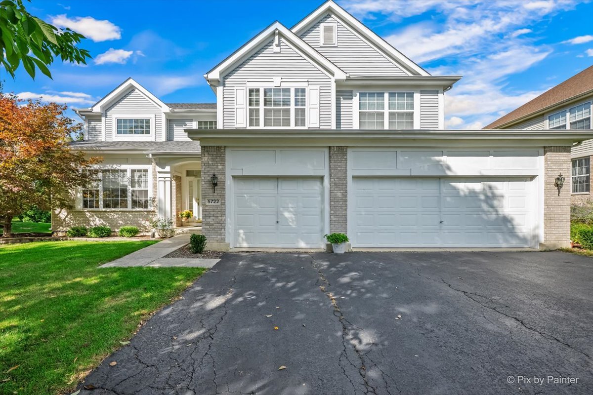 Two-story light-gray house with a three-car garage, stone accents, and a broad driveway.