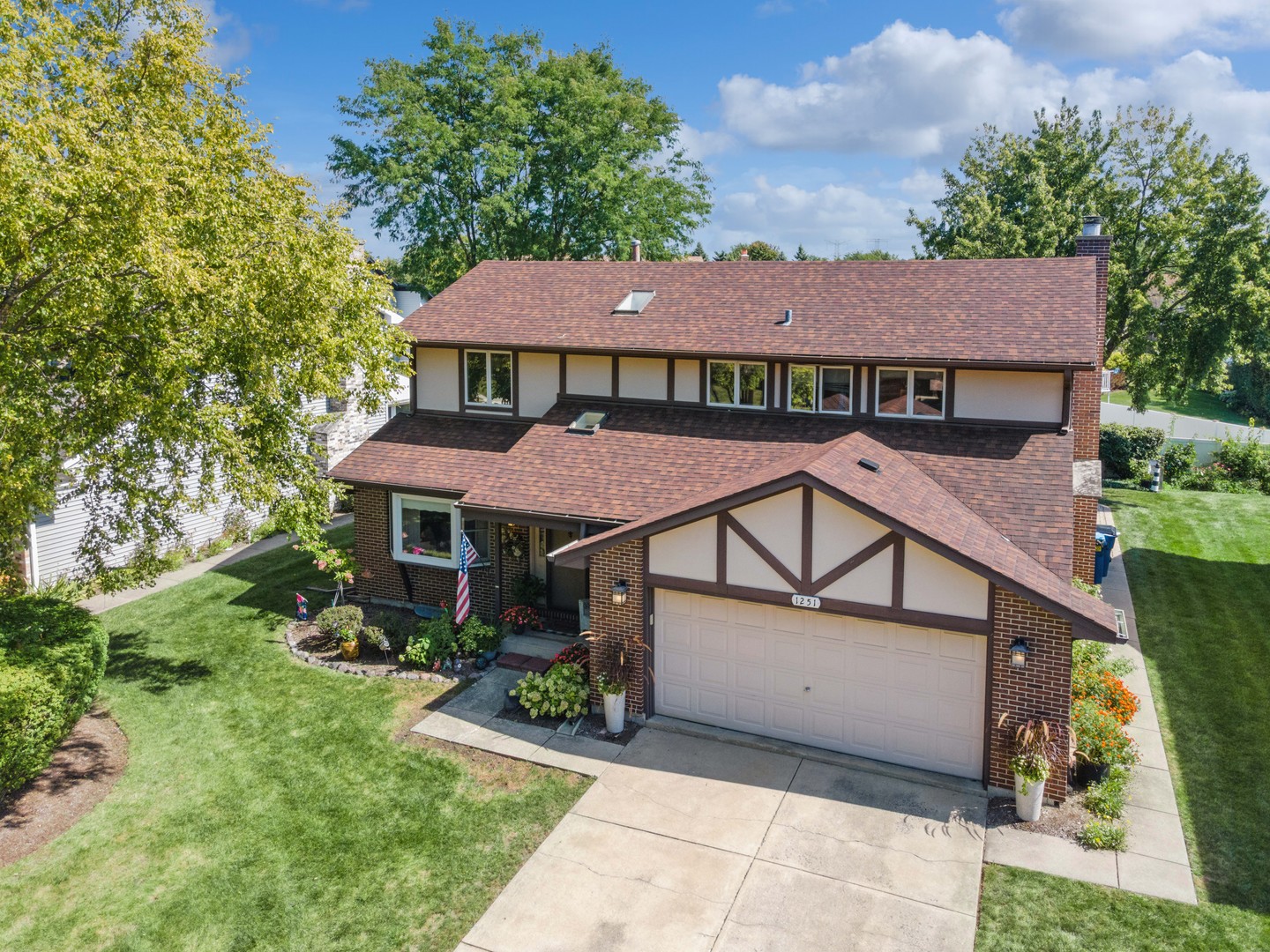 Two-story brick and half-timbered home with an attached garage, landscaped lawn, and mature trees.