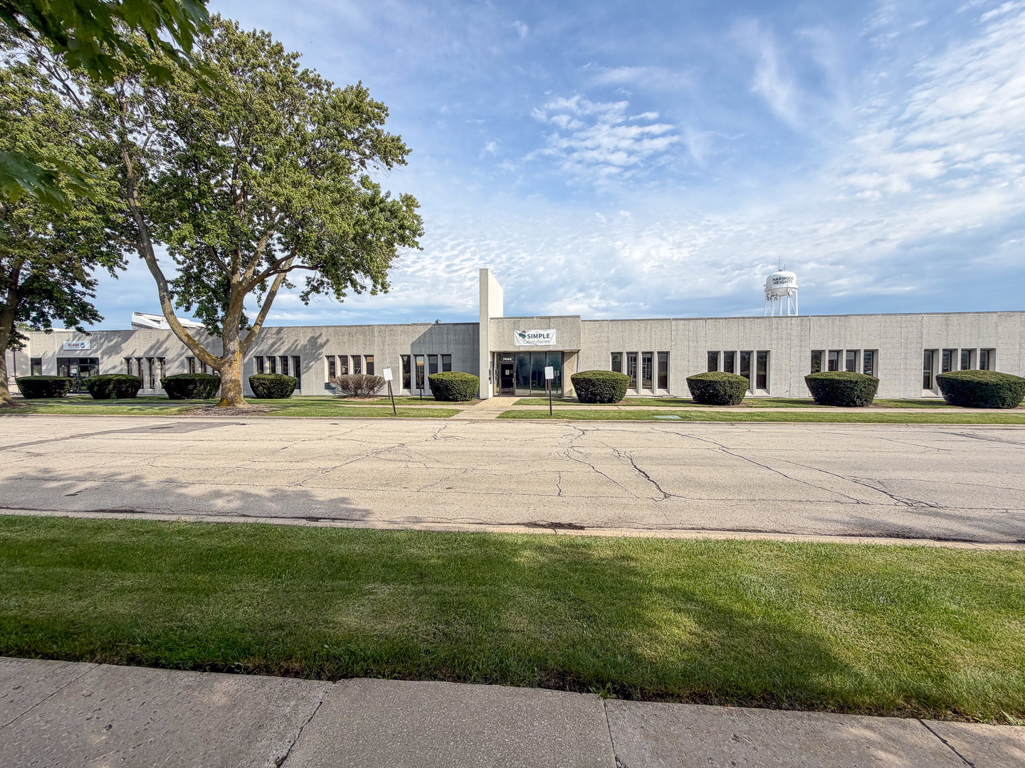Low-rise commercial building in Harwood Heights, with a leafy tree and the town water tower behind it.