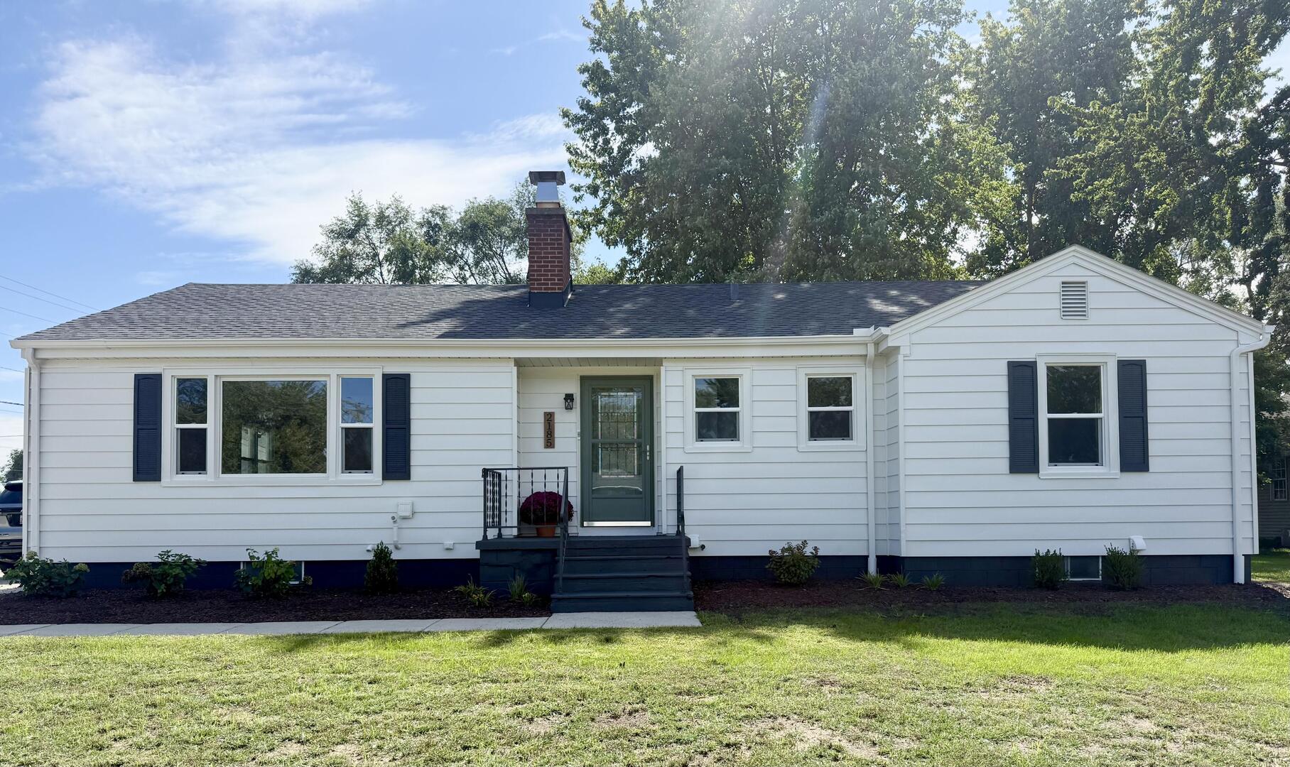 White ranch-style home with dark shutters, brick chimney, and raised front entry porch.