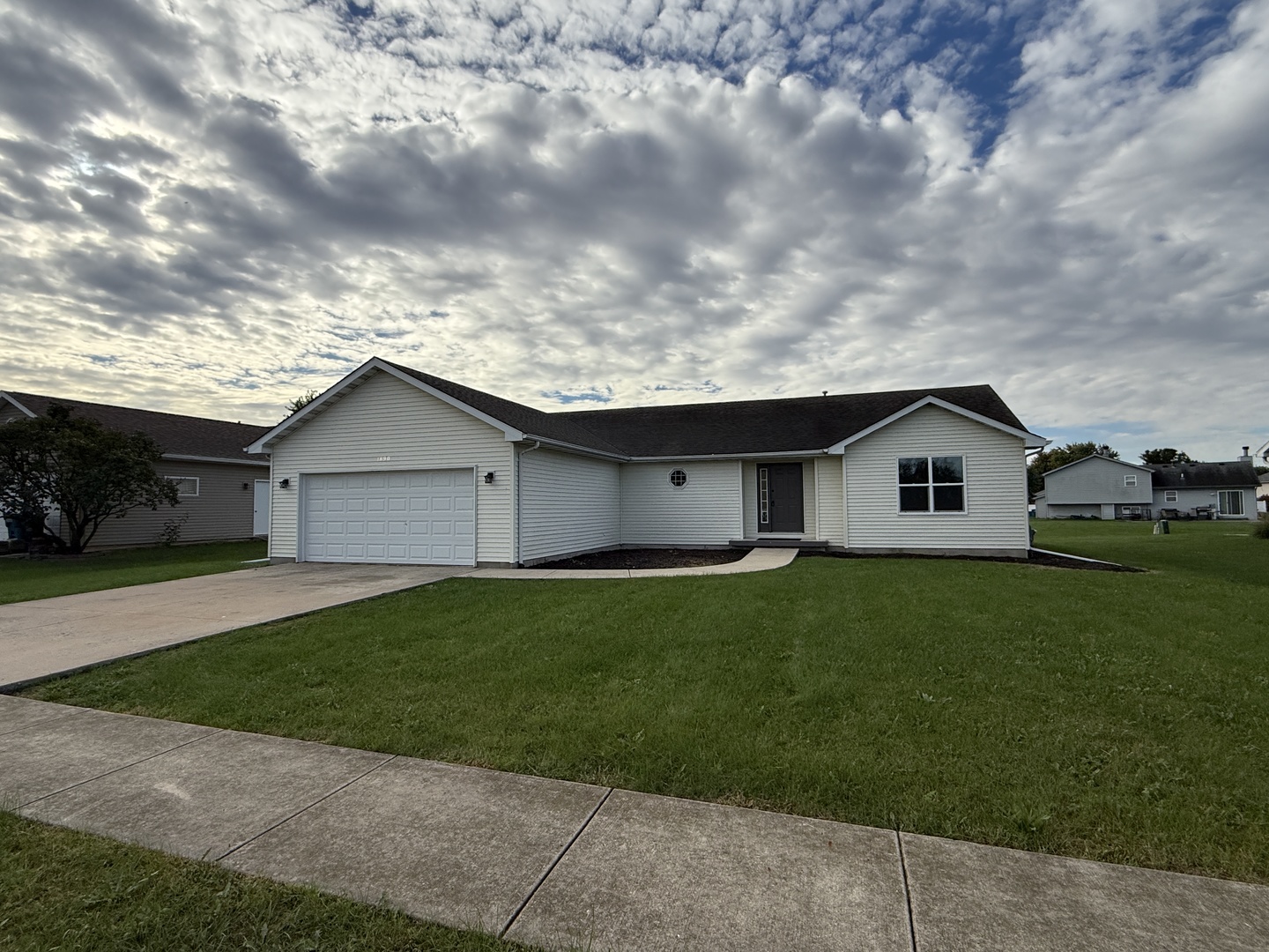 Single-story white house with an attached garage, concrete driveway, and broad front lawn.