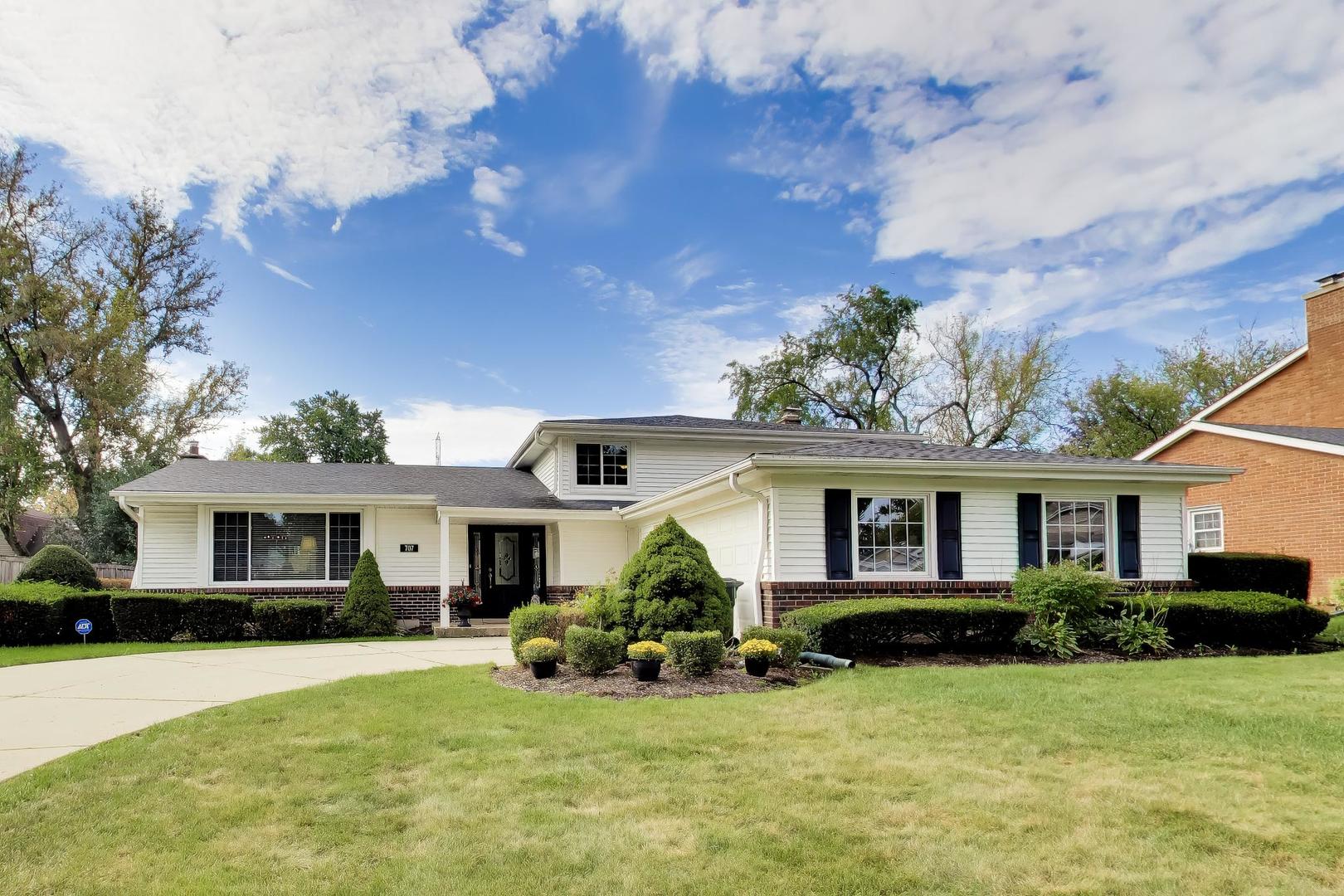 White-sided suburban home with dark brick trim, landscaped flower beds, and a broad front lawn.