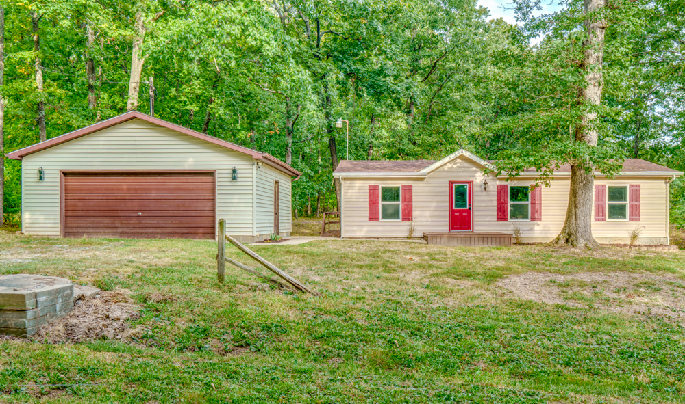 Single-story home with a red front door and detached garage amid mature trees.