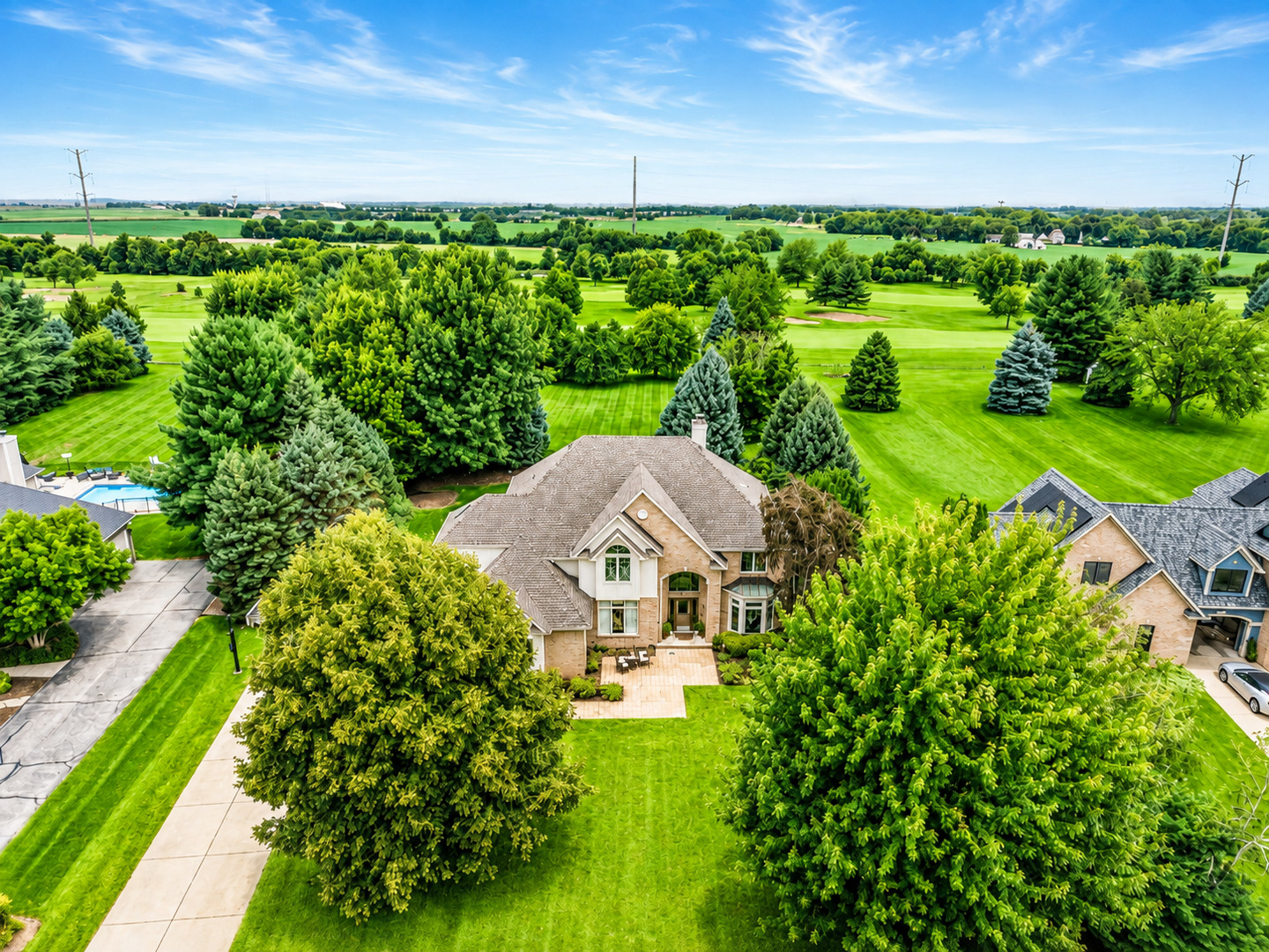 Aerial view of a suburban home beside a golf course, with mature trees and expansive green lawns.