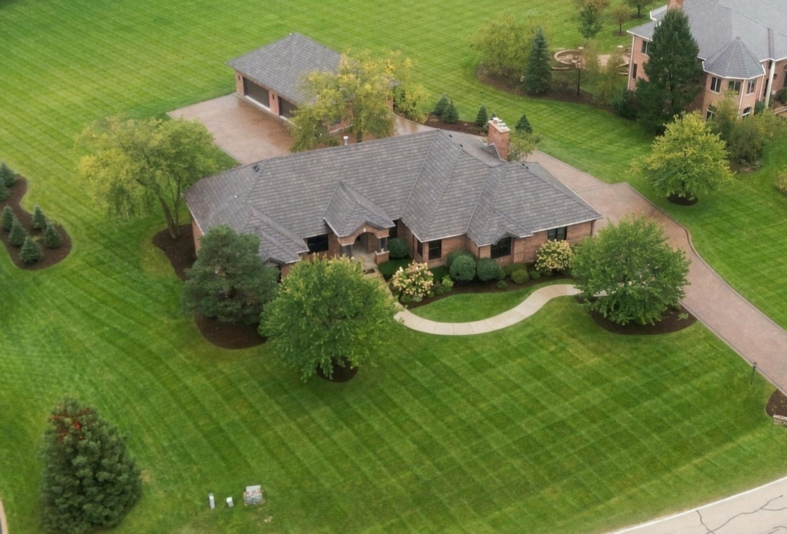 Aerial view of a brick home with a broad lawn, mature trees, and a curved front walk.
