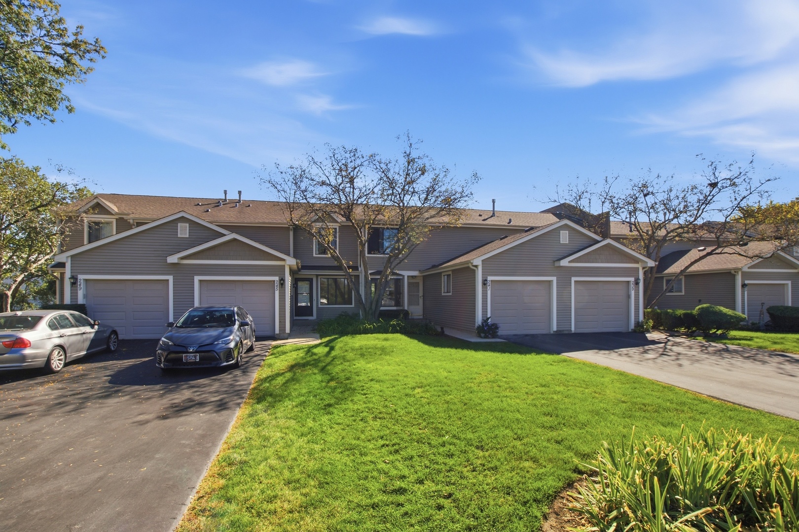 Attached gray homes with white garages, parked cars, and a green lawn.