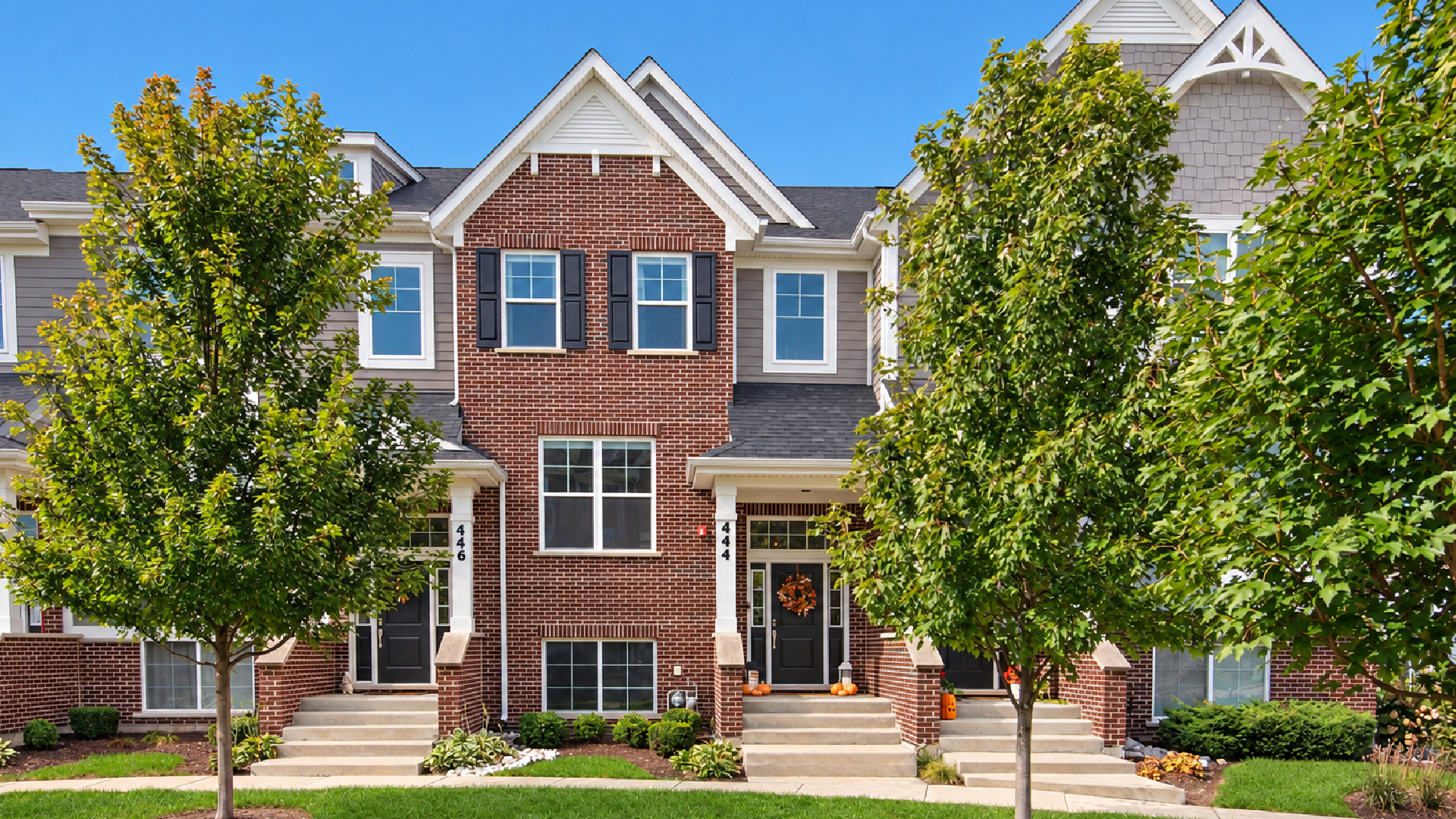 Attached brick townhouses with gray siding, steep gables, and autumn decorations by the front doors.