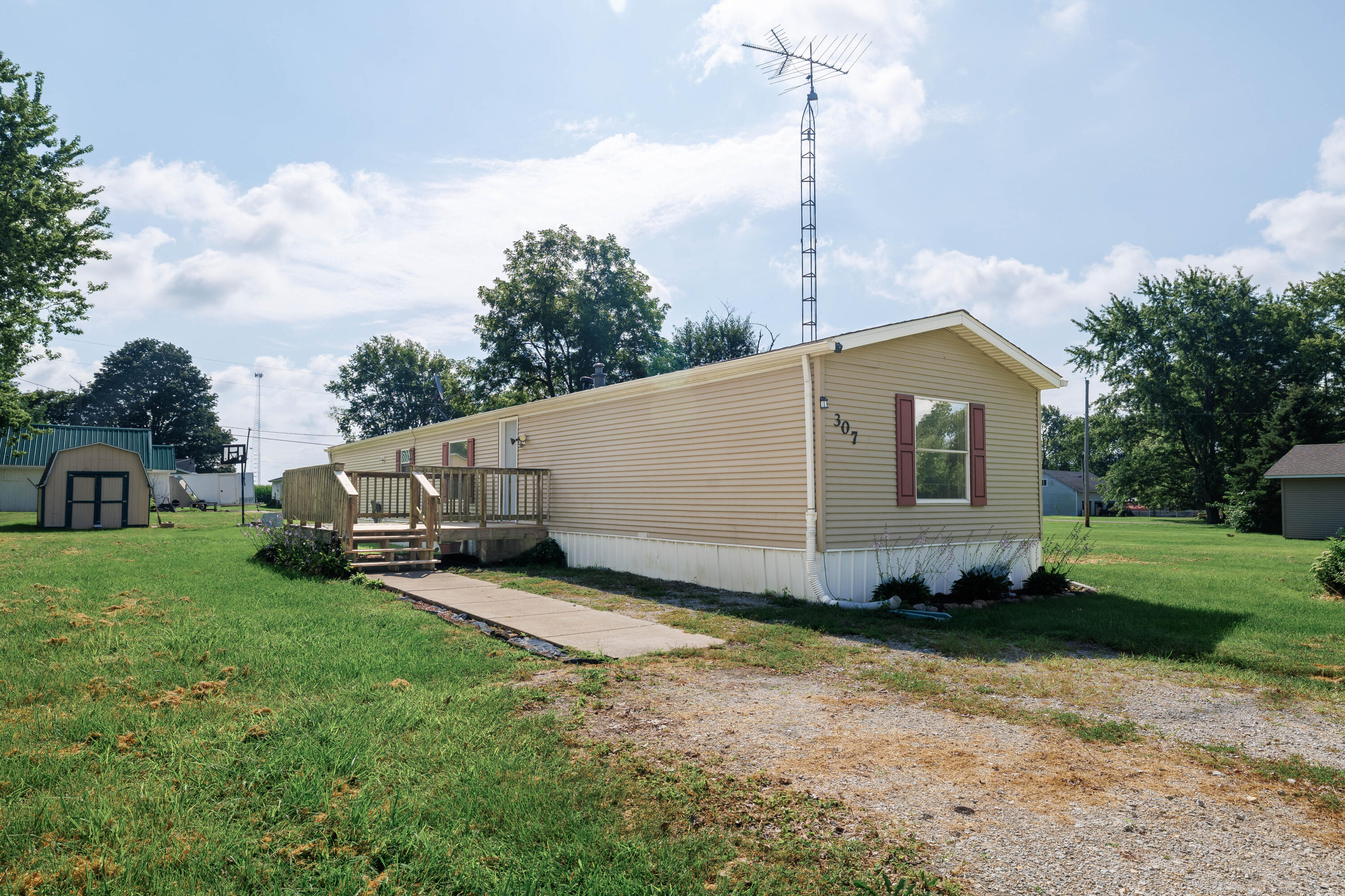 Beige manufactured home with burgundy shutters, a raised wooden deck, and a tall antenna.