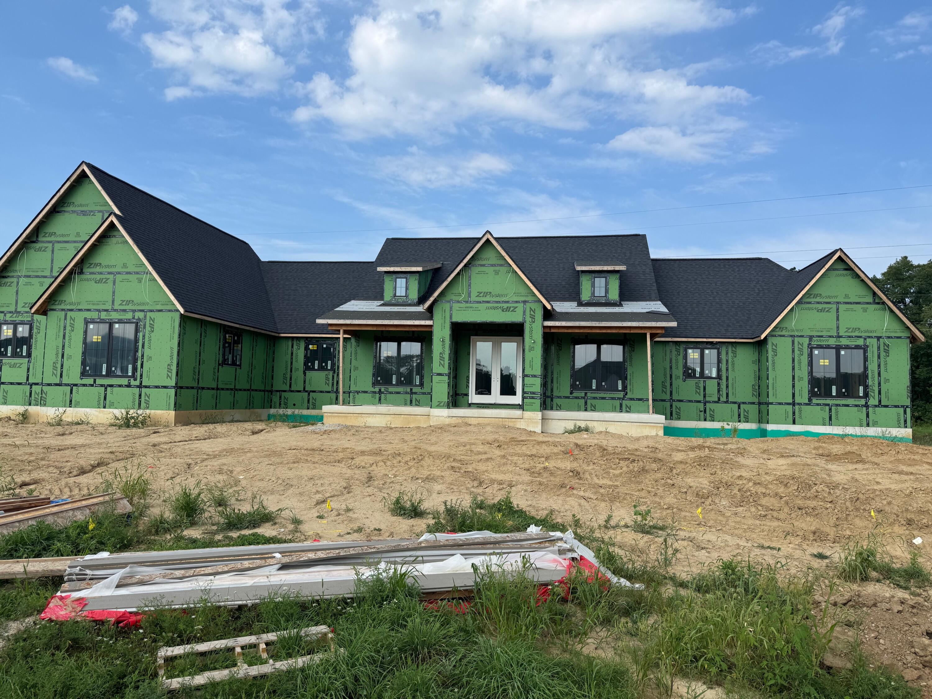Large house under construction with green sheathing, dark gabled roof, and unfinished dirt yard.