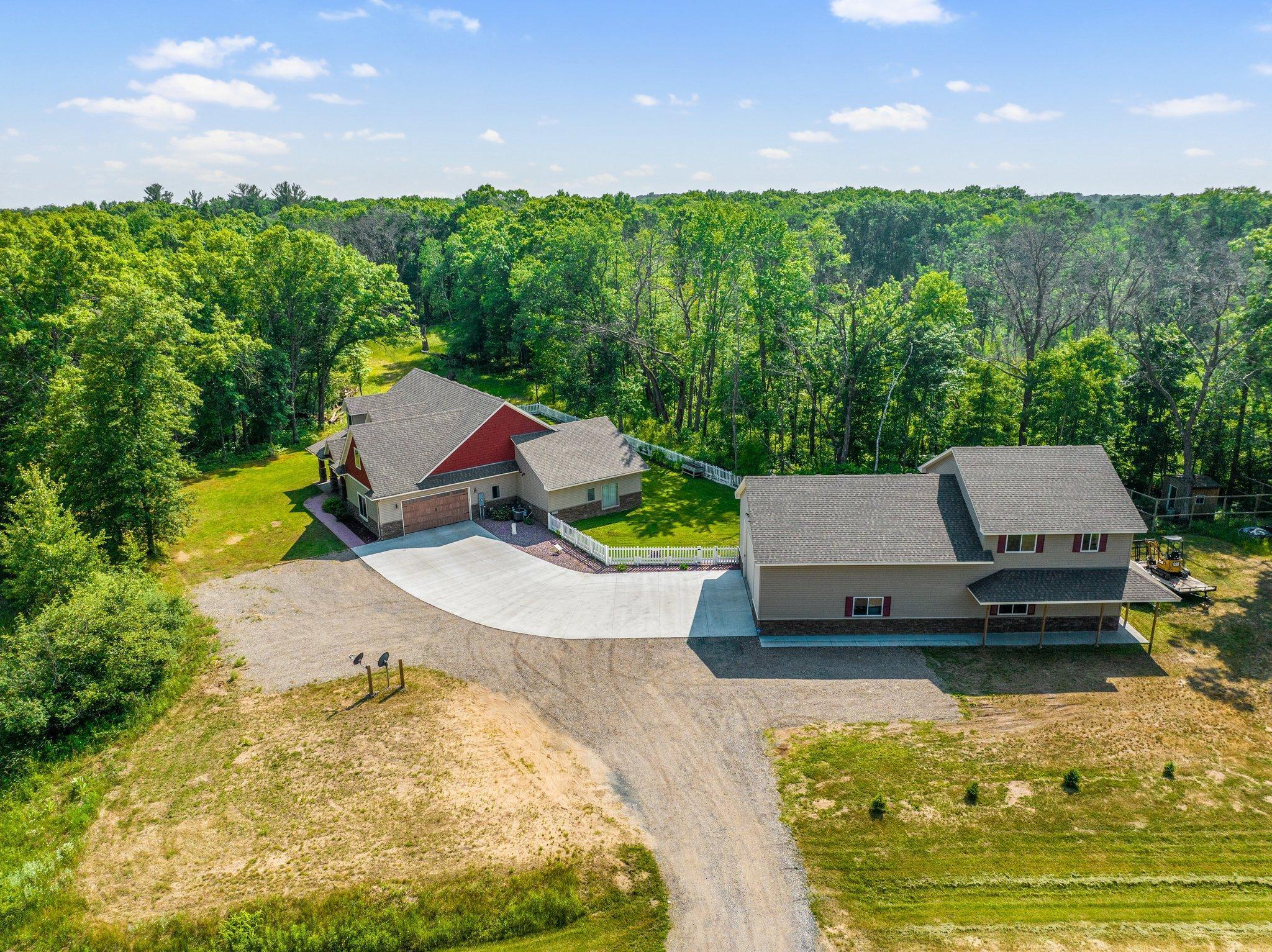 Aerial view of two homes connected by a curved driveway, surrounded by trees.