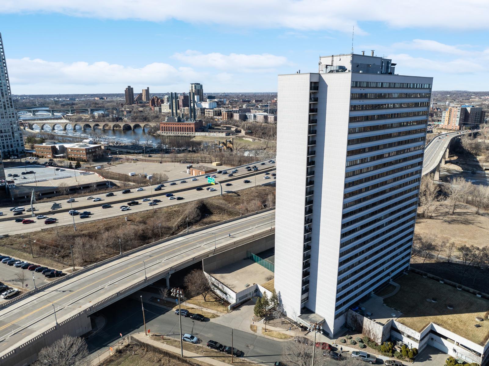 Aerial city view with a river, bridges, highway interchange, and prominent white high-rise.