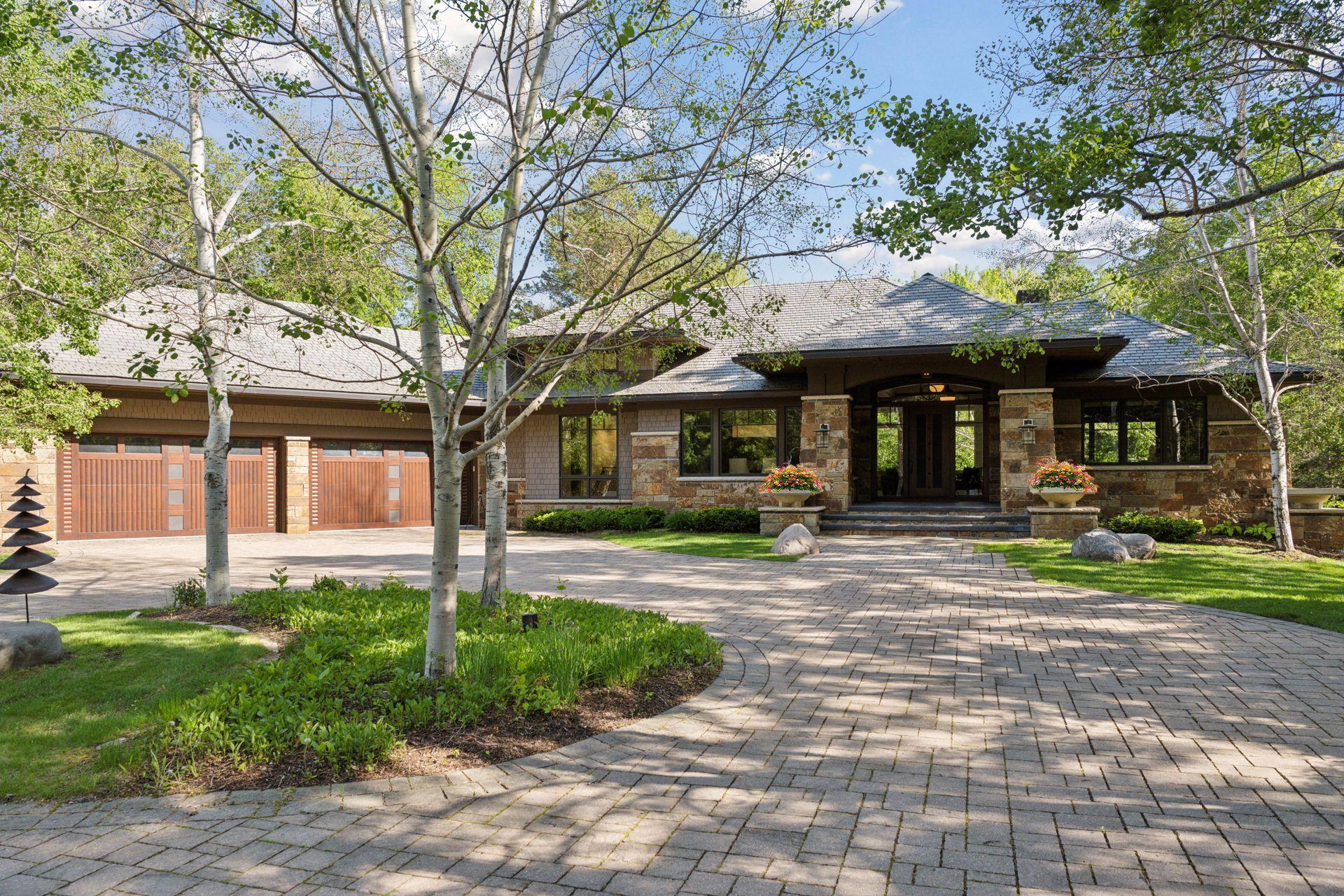 Luxury home with stone facade, broad driveway, and landscaped entrance beneath leafy trees.