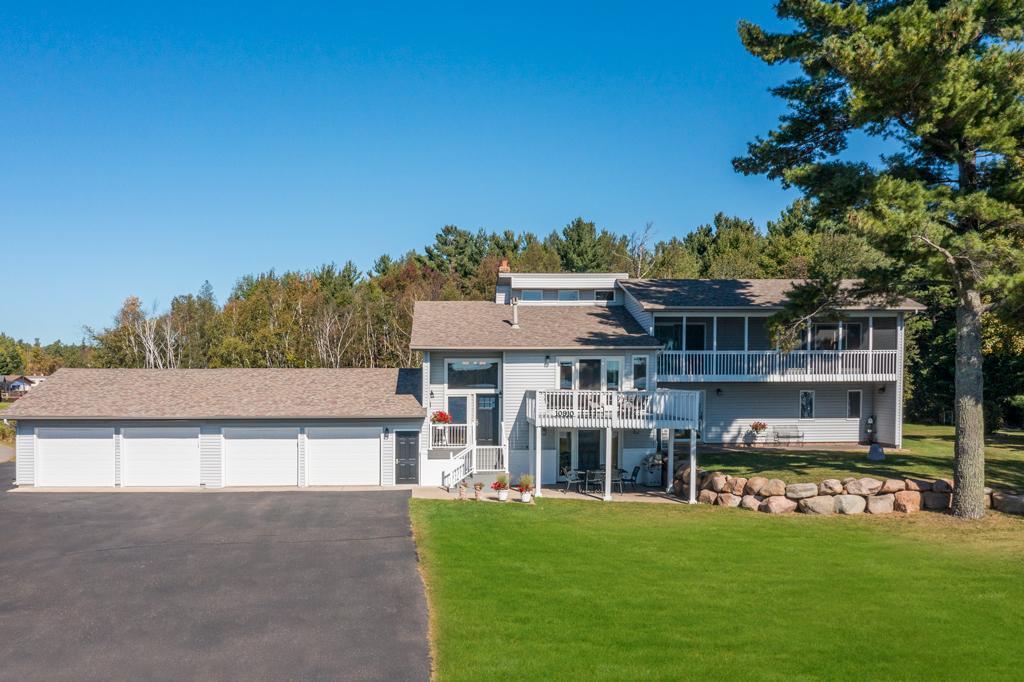 Gray two-story home with a long four-car garage, elevated deck, and broad lawn.