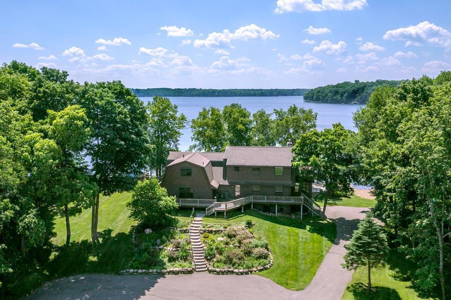 Lakeside home framed by mature trees, with a landscaped lawn and lake beyond.