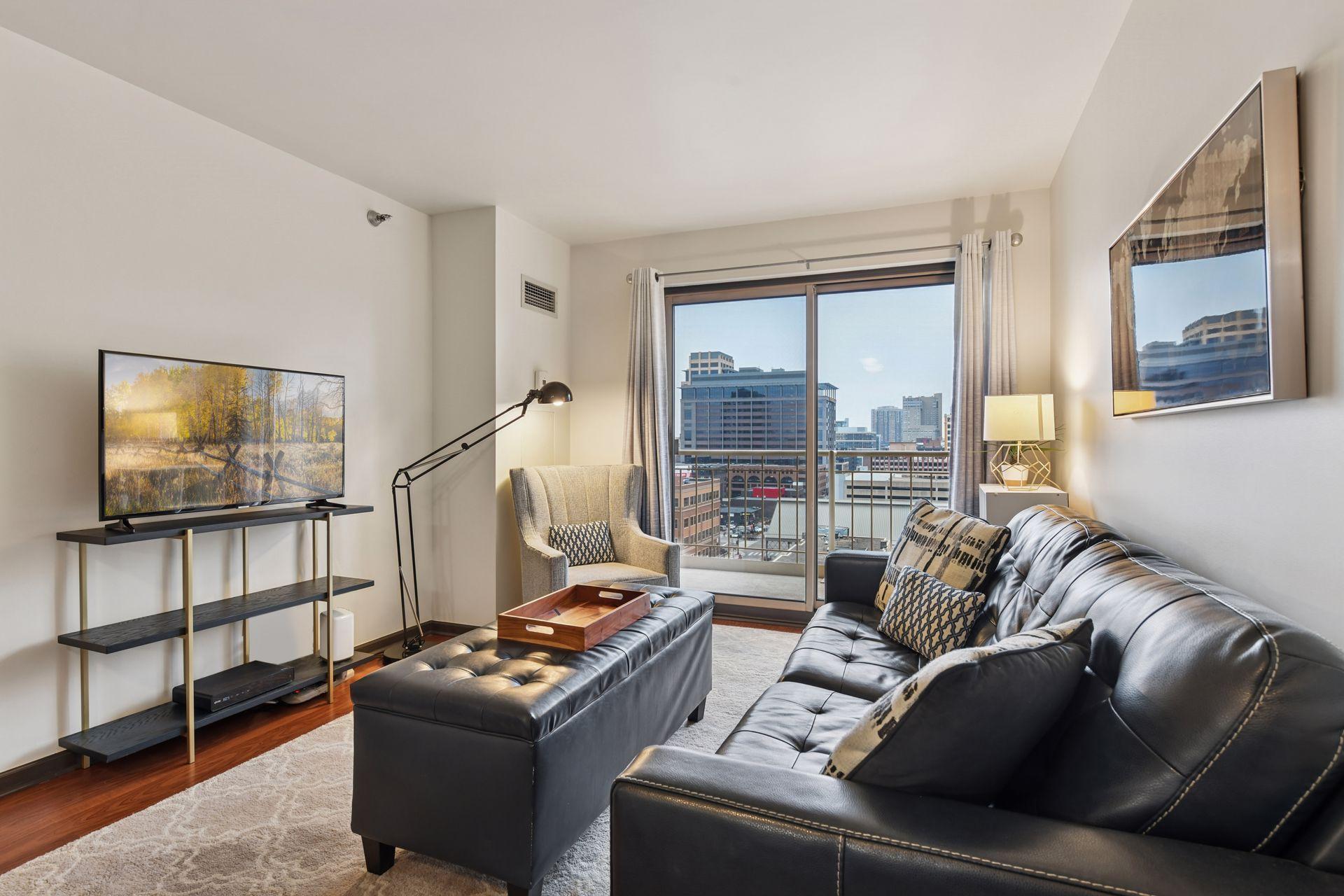 Living room with black leather sofas and a balcony overlooking downtown buildings.