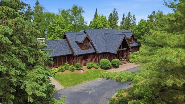 Log-style home with a gray shingle roof and curved driveway, surrounded by trees.