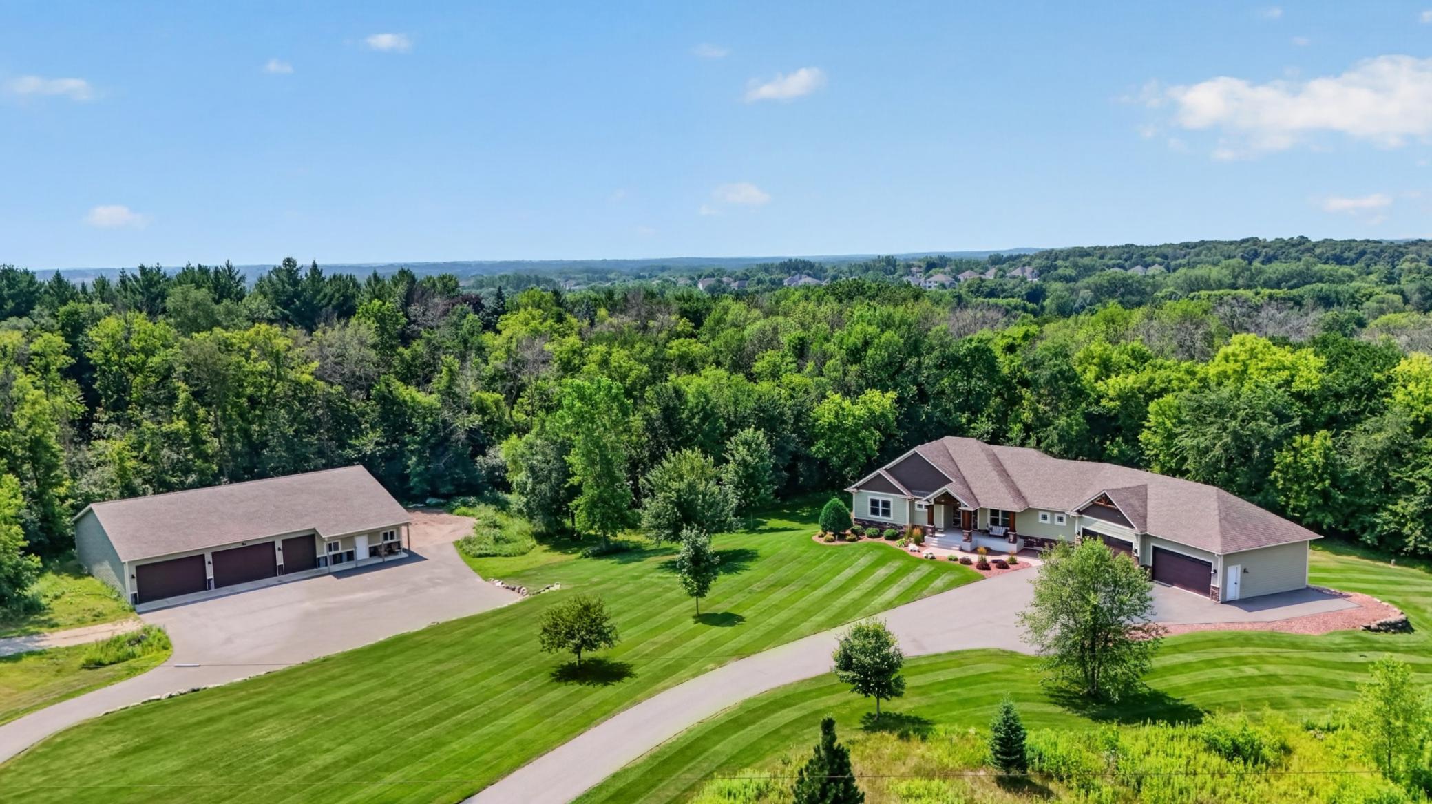 Aerial view of a home, detached garage, striped lawn, and surrounding trees.