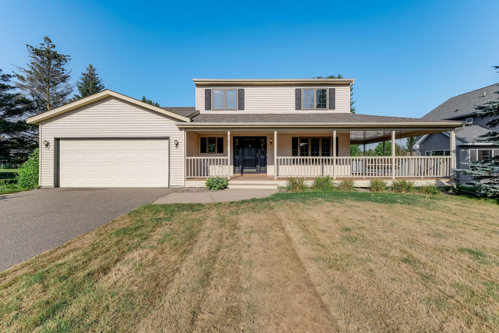 Two-story beige home with a large garage and long covered front porch.