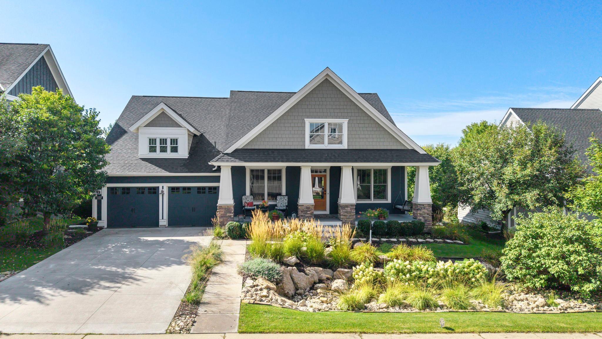 Gray two-story house with a covered porch, attached garage, and landscaped rock garden.