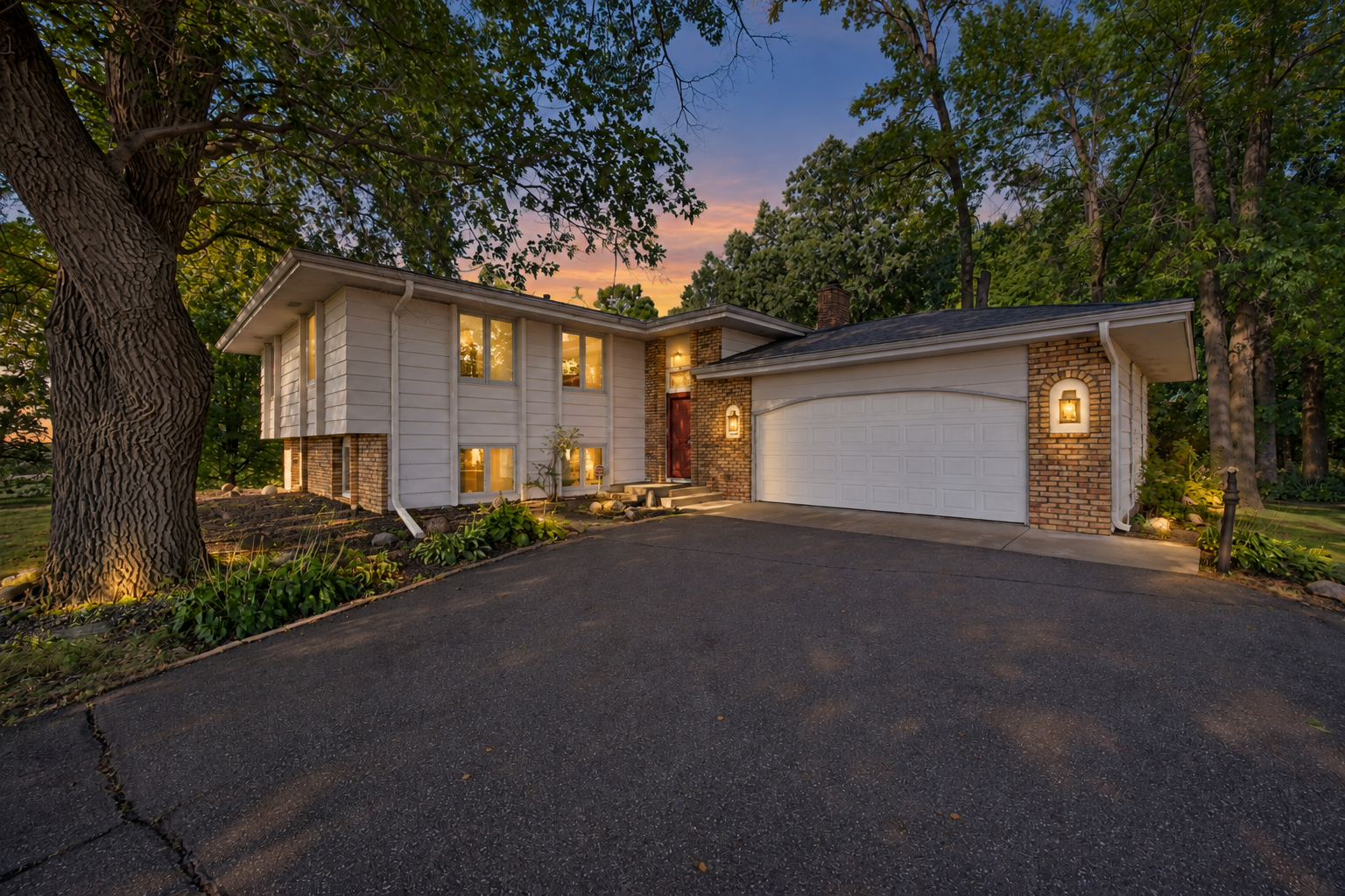 Split-level home with brick accents and an attached garage, framed by mature trees at dusk.