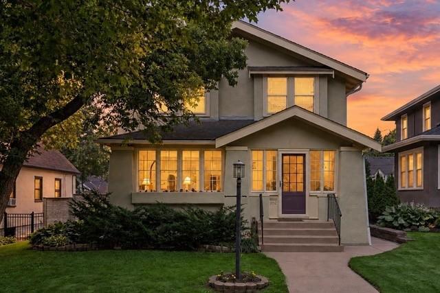 Gray gabled house with a purple front door and warmly lit windows at dusk.