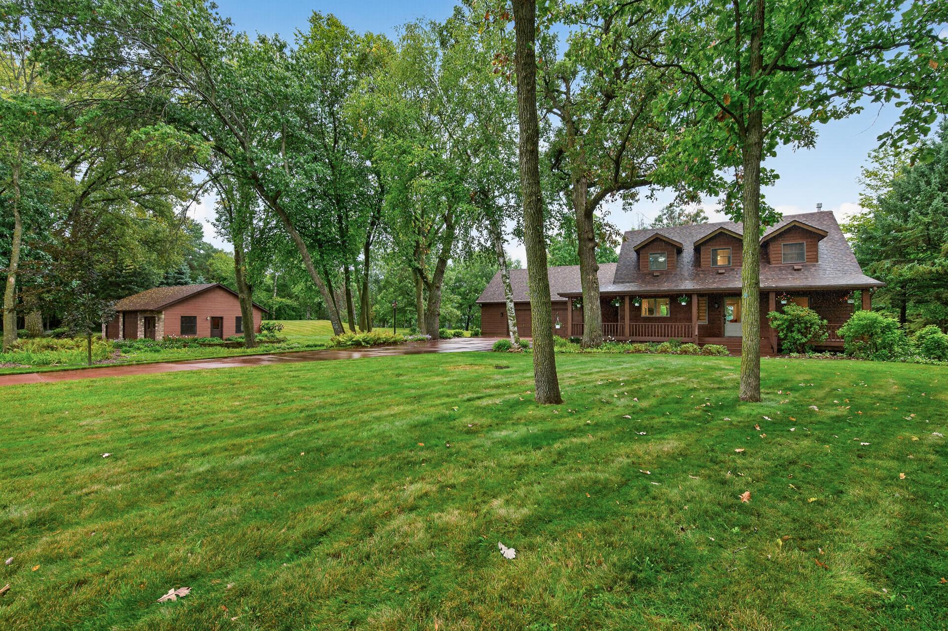 Brown home with a covered porch and three dormers, surrounded by mature trees and a broad lawn.