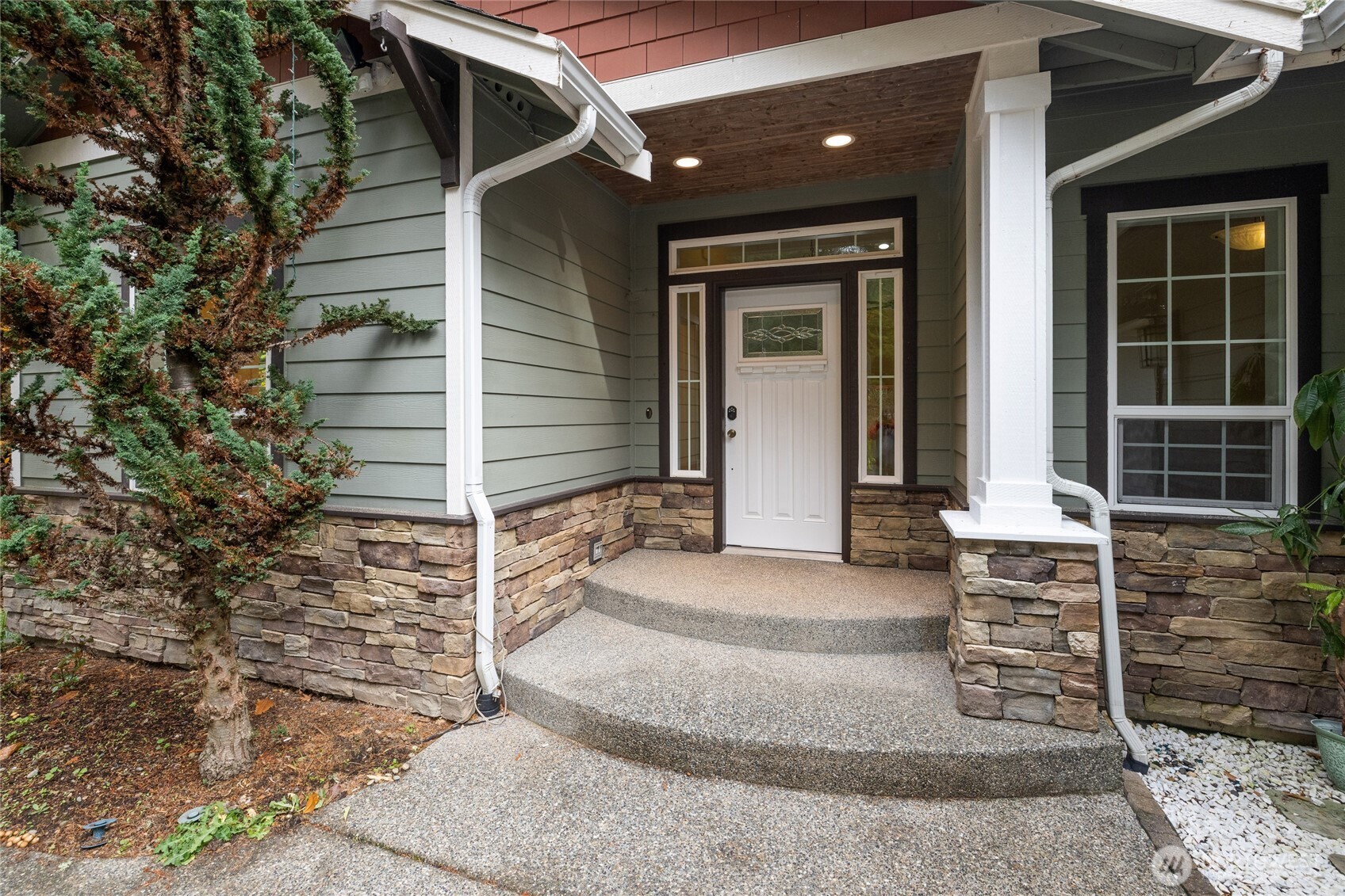 Covered home entrance with a white door, stone veneer, and broad concrete steps.