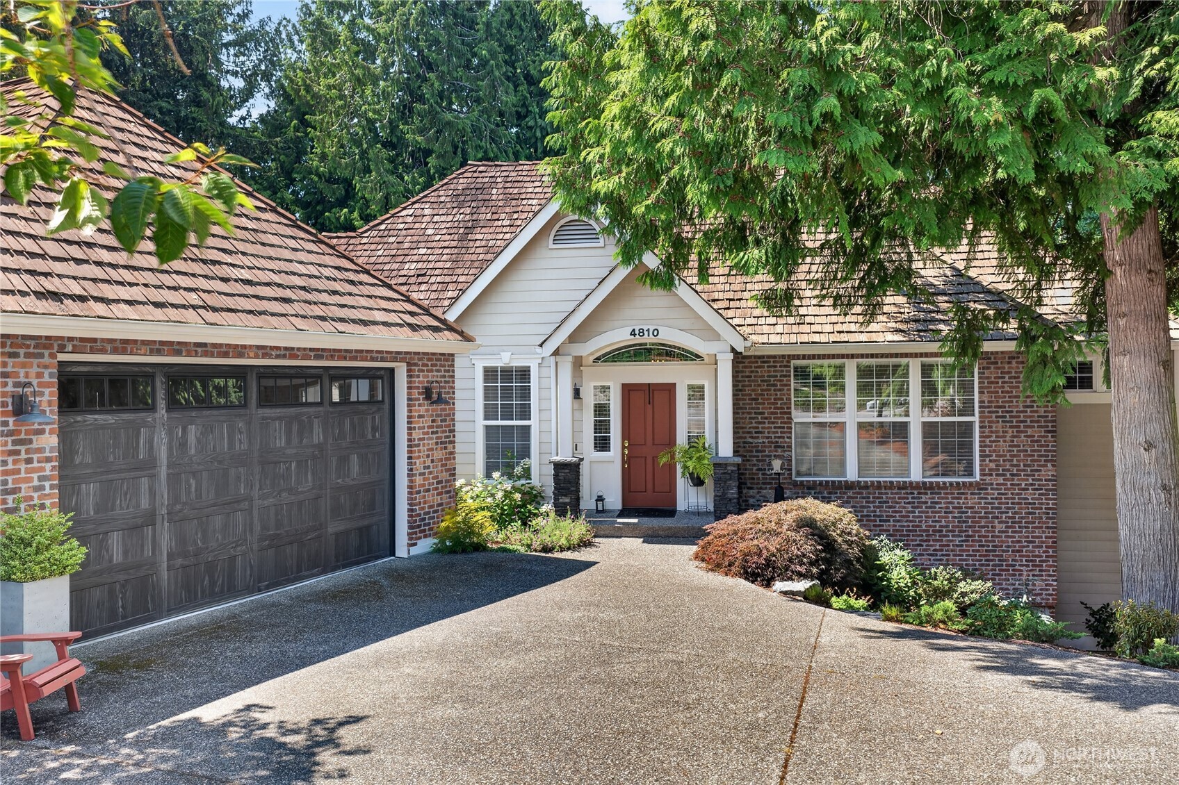 Brick house with a red front door and broad driveway, shaded by mature trees.