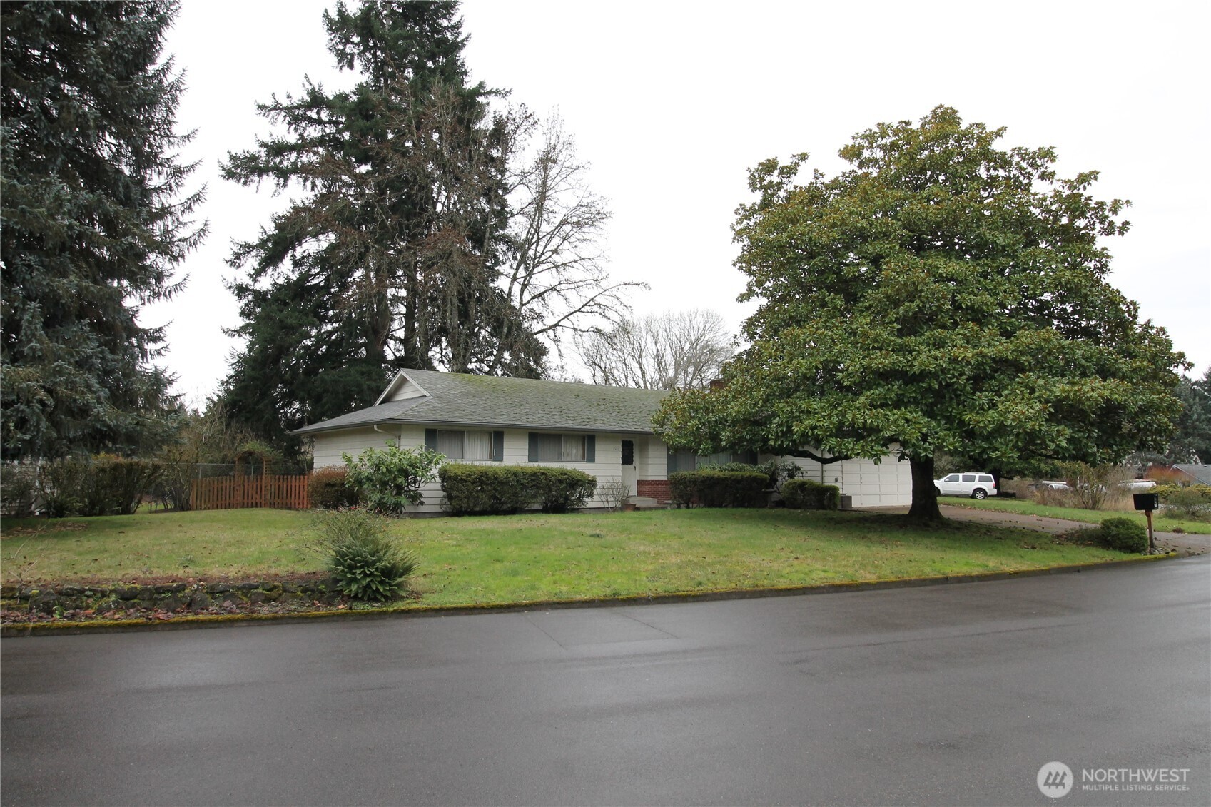 Single-story house with an attached garage, broad lawn, and a large tree partly obscuring the garage.