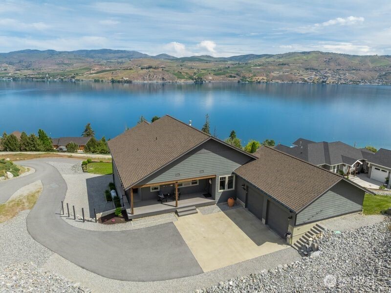 Aerial view of a gray-green home with a covered patio and driveway overlooking a lake.