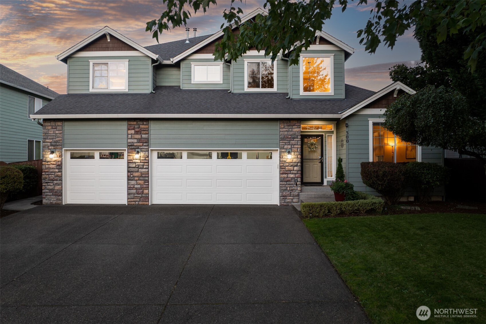 Green two-story house with stone accents and two garage doors, photographed at dusk.