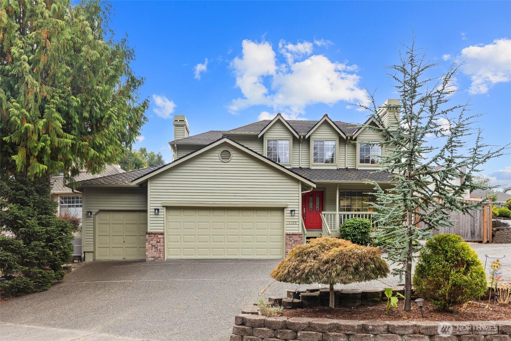 Two-story sage-green house with a red front door, double garage, and landscaped front yard.