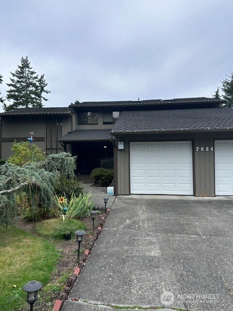 Two-story dark-sided home with a white garage door, landscaped entry, and wide concrete driveway.
