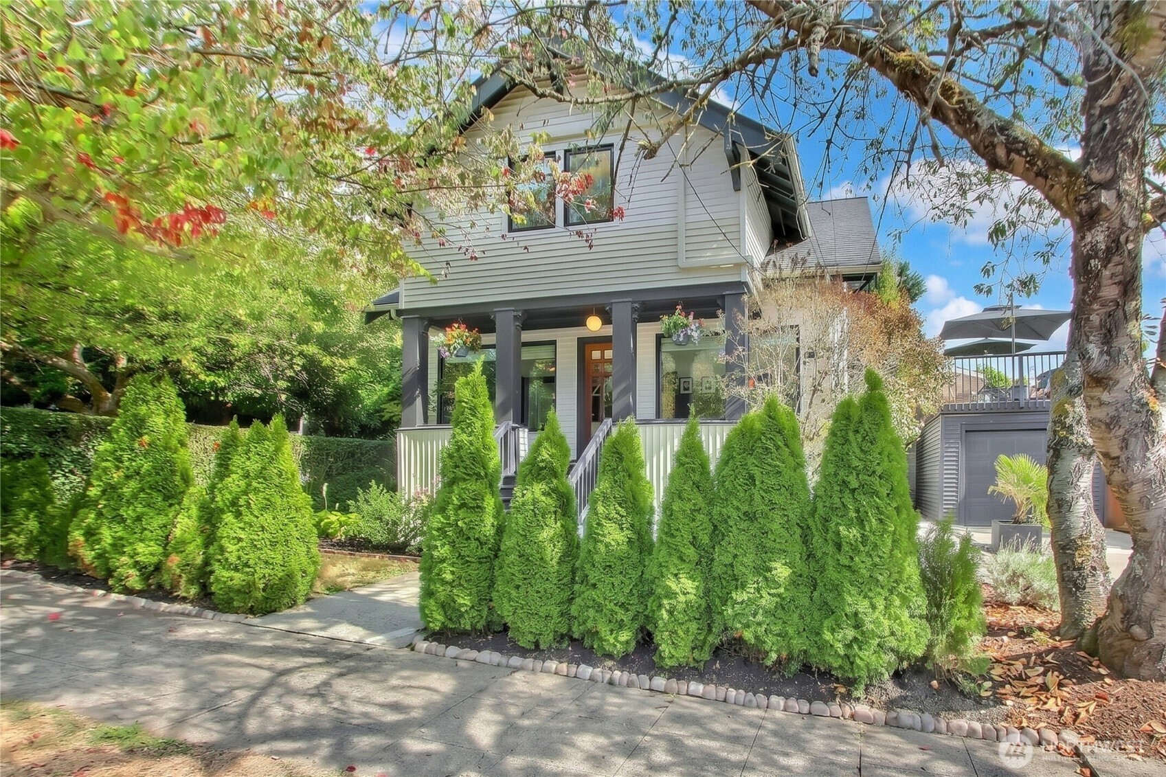 Two-story house with a covered porch, evergreen hedges, and a detached garage with a raised deck.