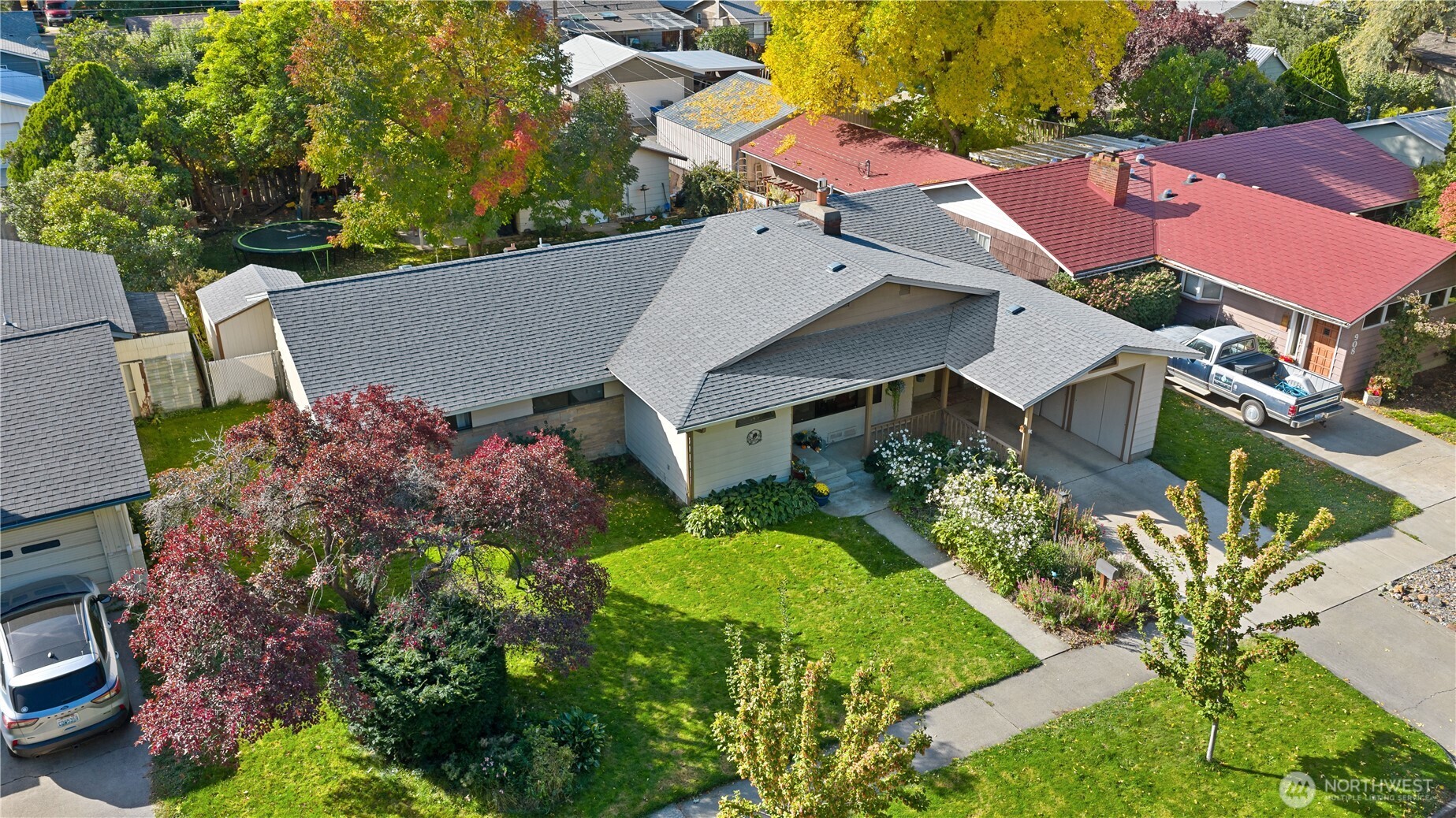 Aerial view of a single-story home with a gray roof, landscaped lawn, and surrounding autumn trees.