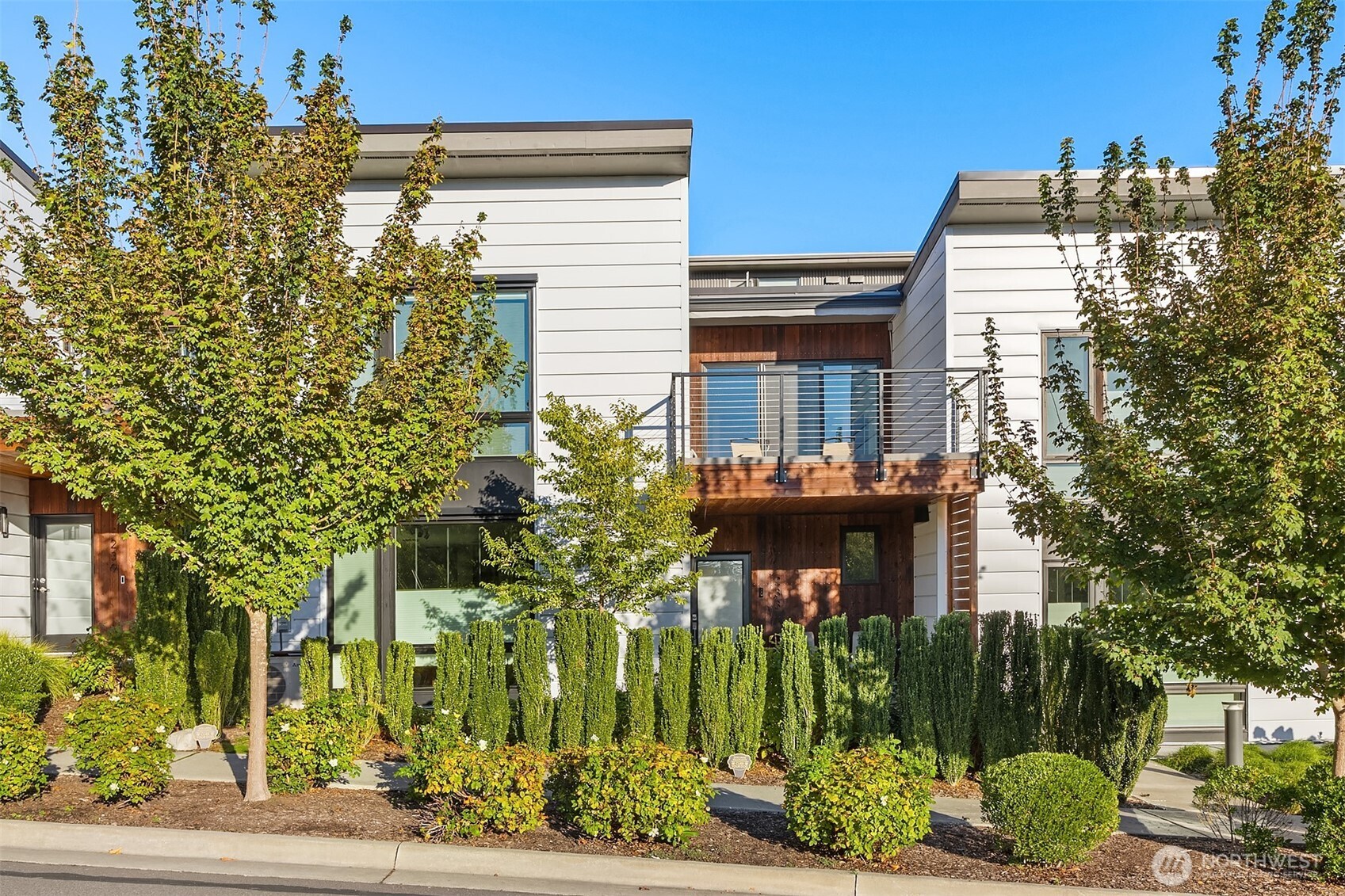 Contemporary home with a wood-accented balcony, large windows, and landscaped frontage.