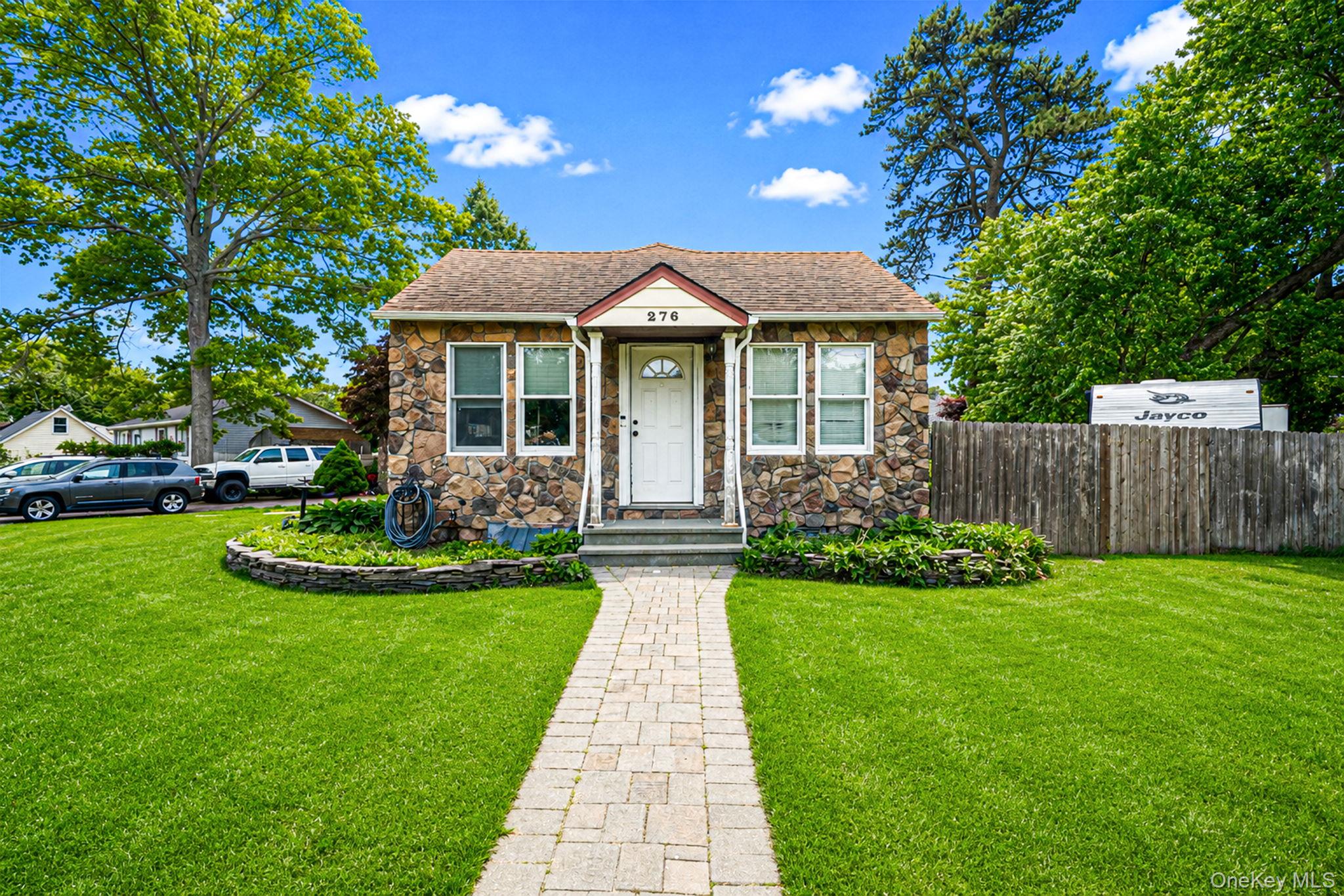 Stone-faced house with a paved front walkway, green lawn, and mature trees.